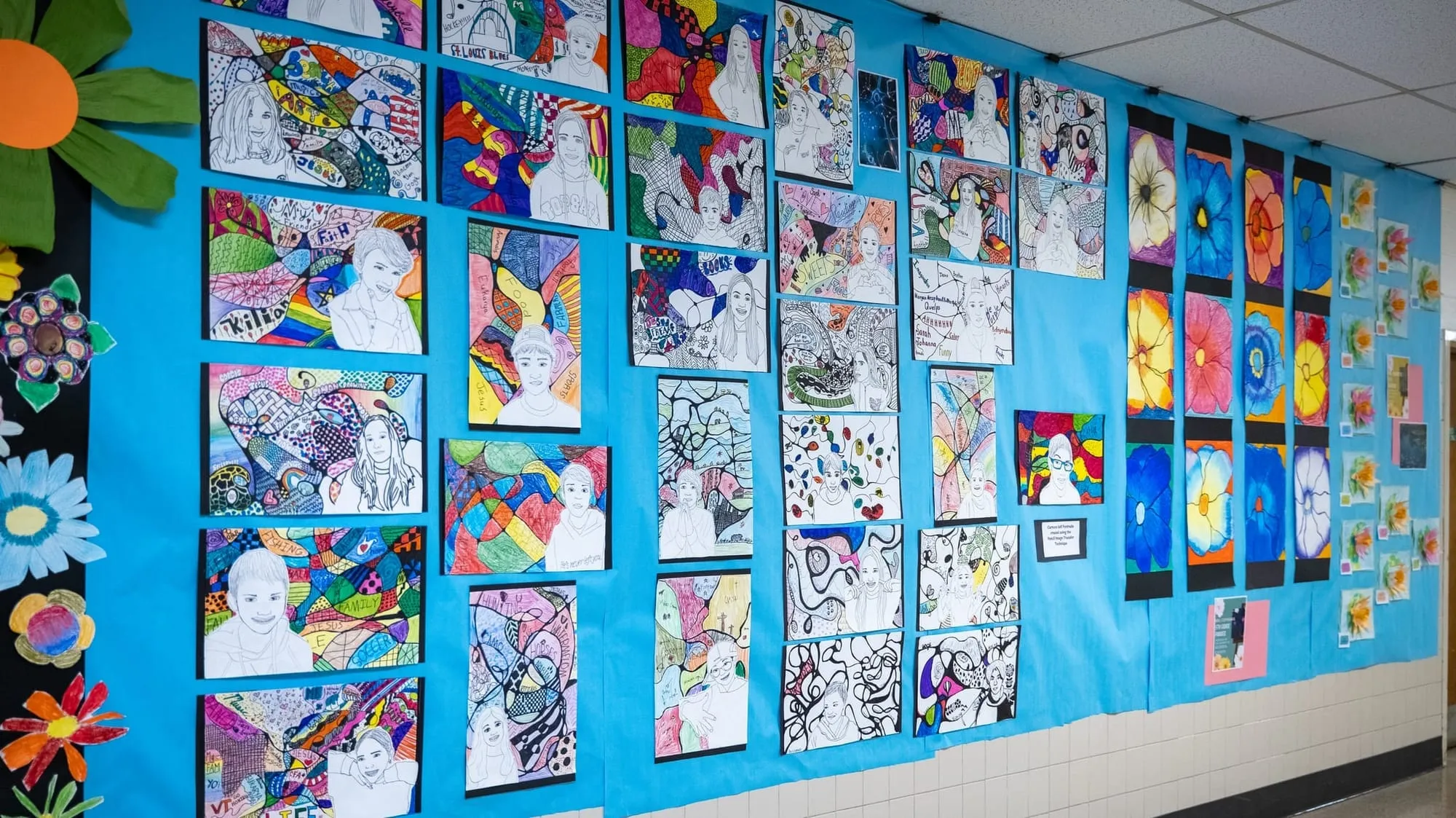 A school corridor lined floor to ceiling with mounted student paintings and drawings on bright blue paper
