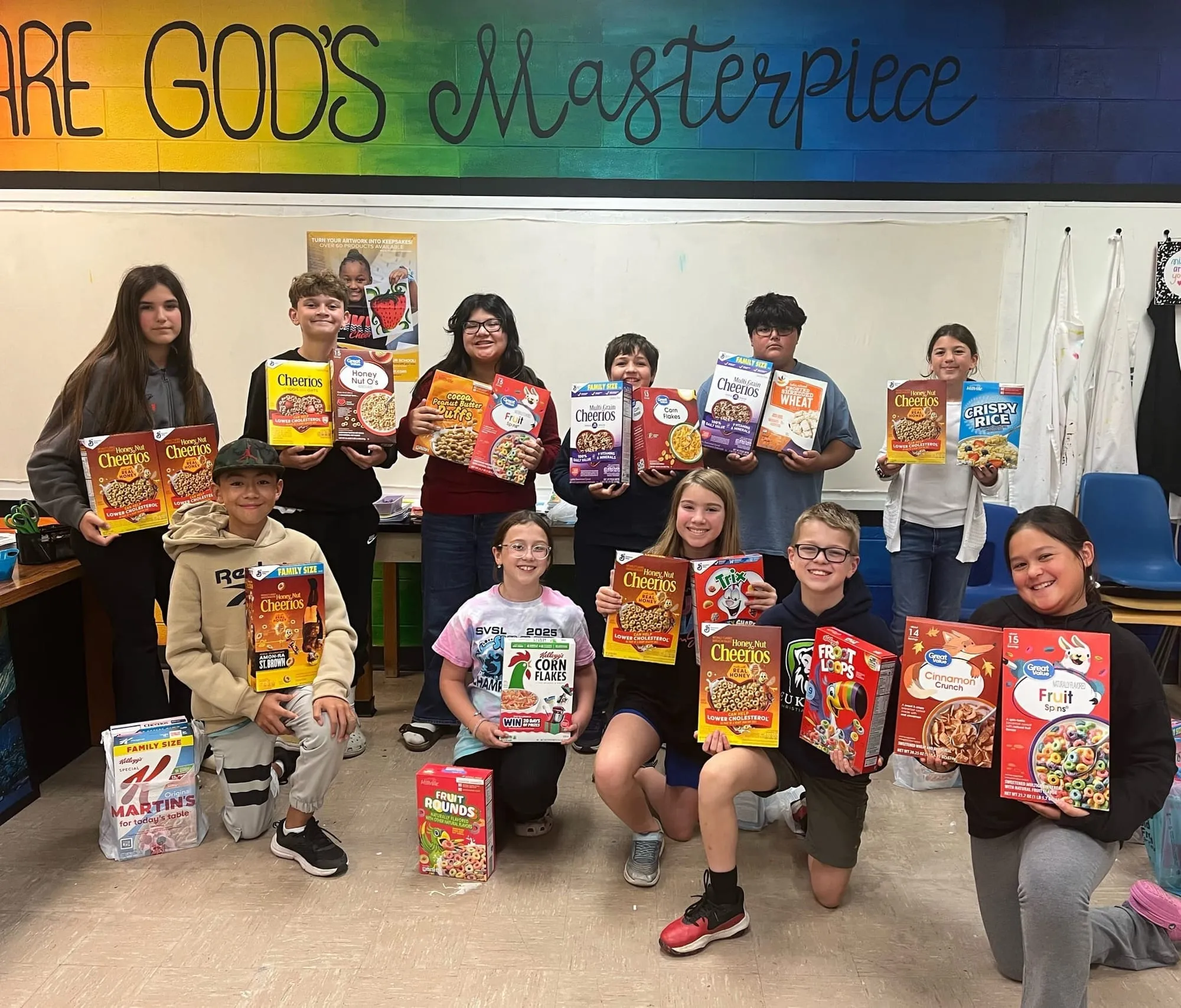Upper school students holding boxes of donated food beneath a hand-lettered banner reading "You are God's masterpiece"