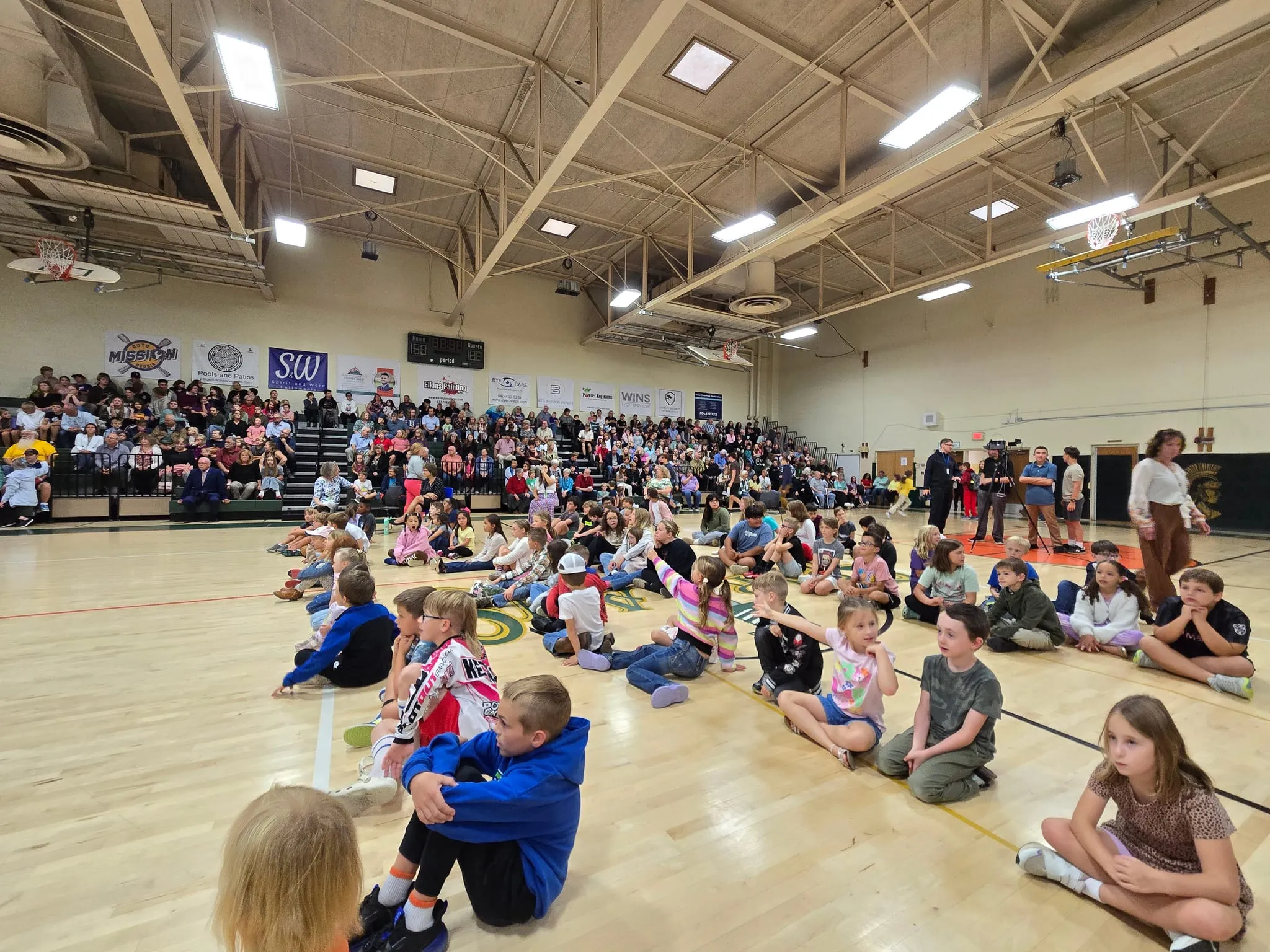 The whole school gathered for morning assembly — younger students seated on the gym floor, older students filling the bleachers behind them