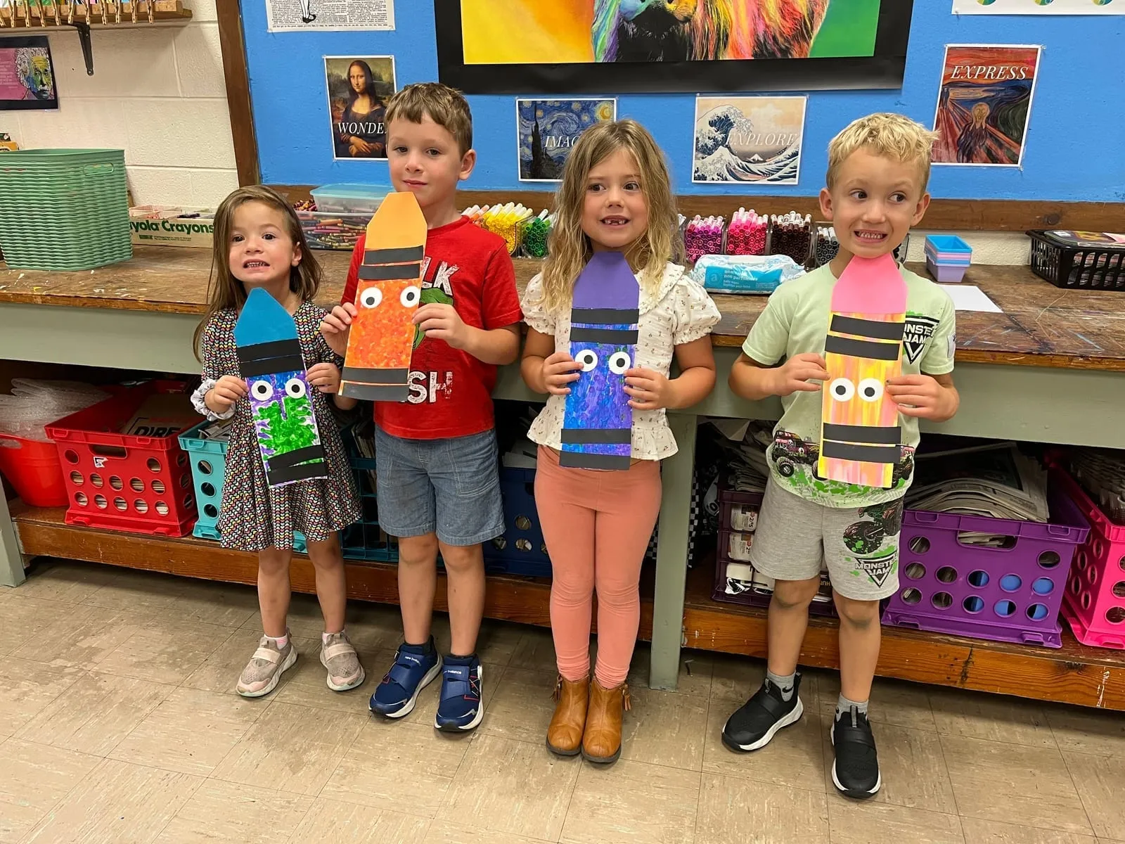 Four kindergarten students standing in the art room holding up the crayon collages they made
