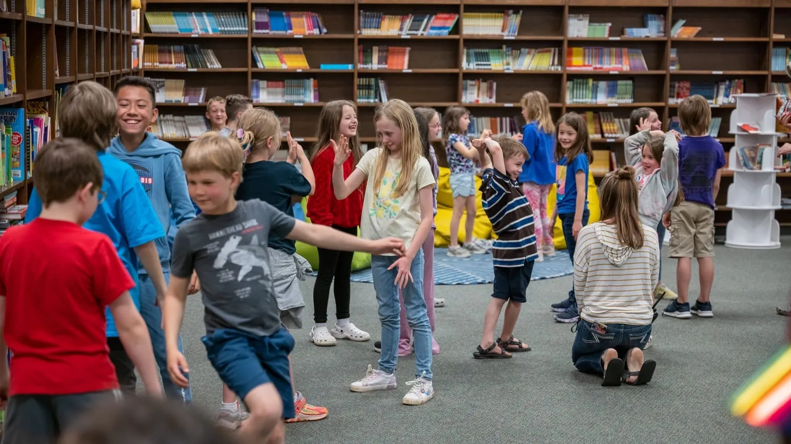 A class mid-game between the library stacks, students moving and laughing