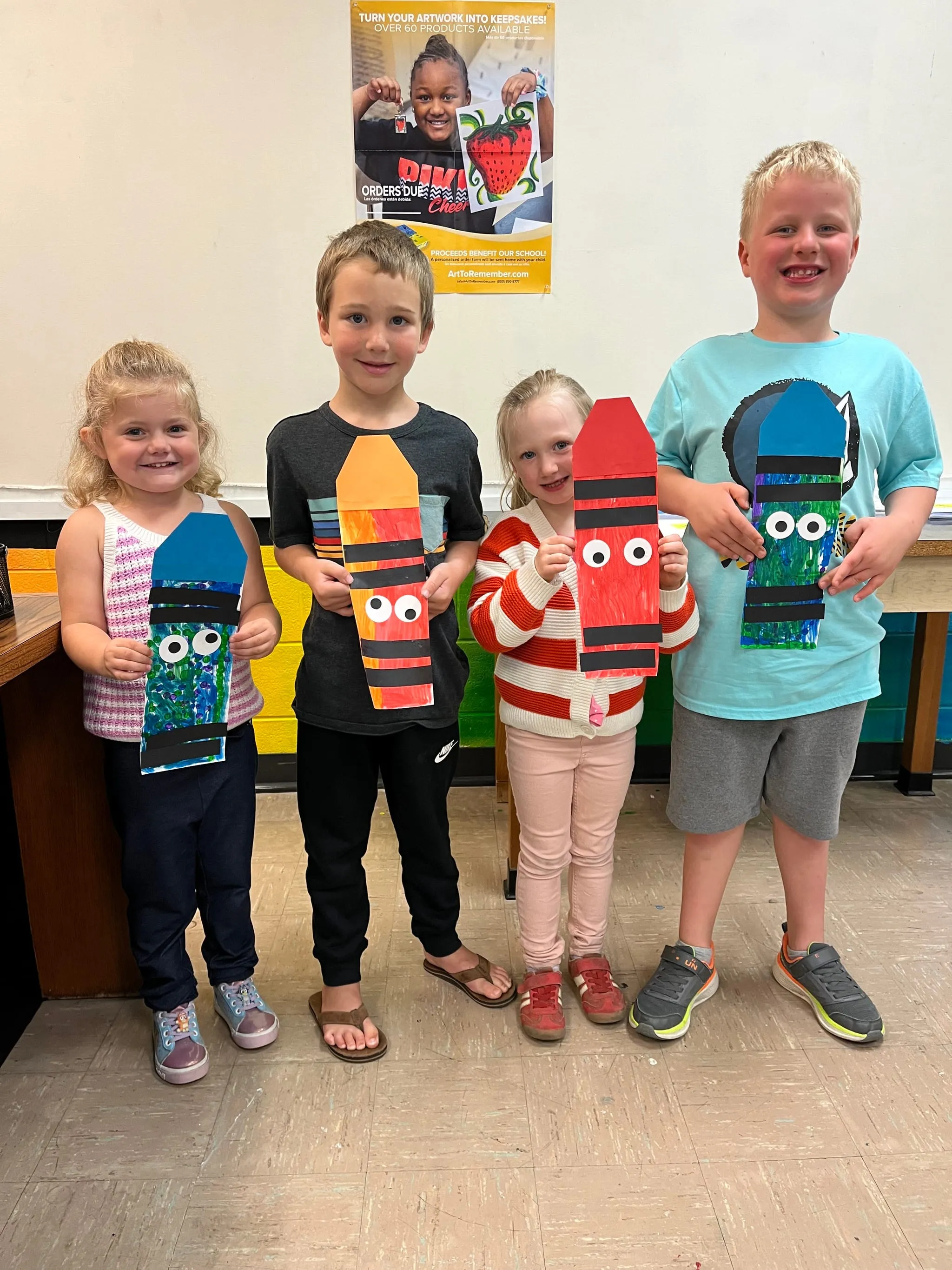 Four young students in the art room holding up the paper collages they finished that morning