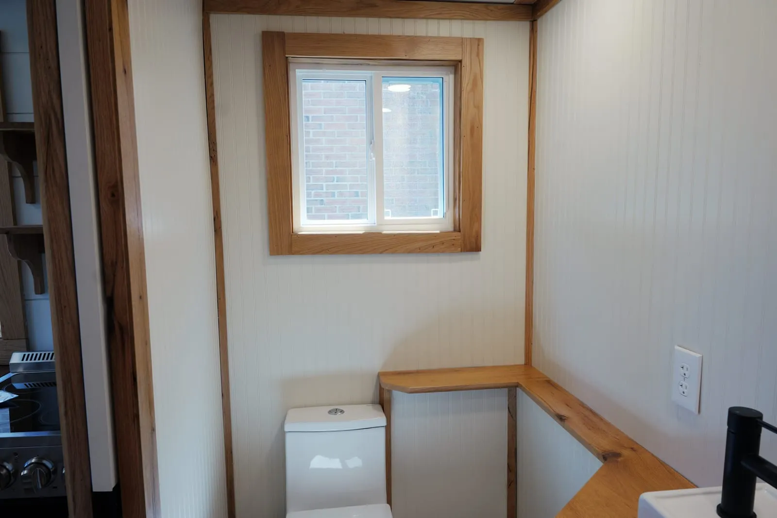 Bathroom with cream beadboard walls, an L-shaped oak counter ledge and a wood-trimmed sliding window above the toilet