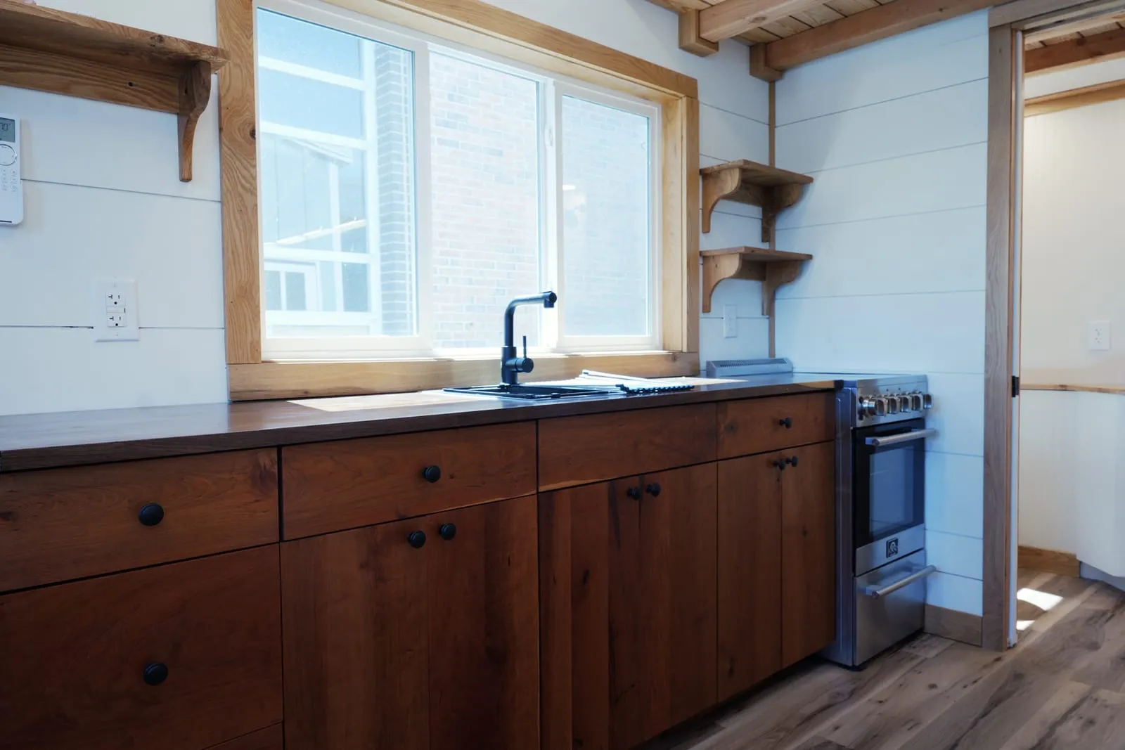 Galley kitchen with cherry cabinets, a black walnut butcher-block counter, open oak shelves on corbels and a stainless Forno range