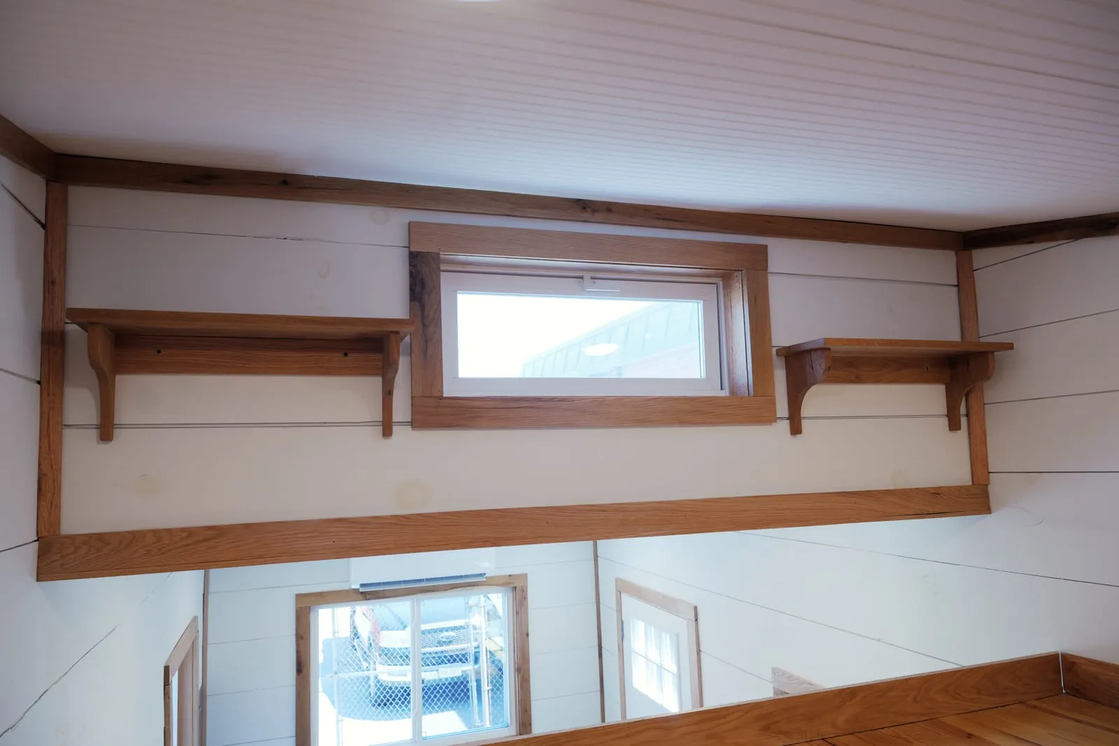 Sleeping loft with a wide sliding transom window, oak shelves on corbels either side and knotty pine floors