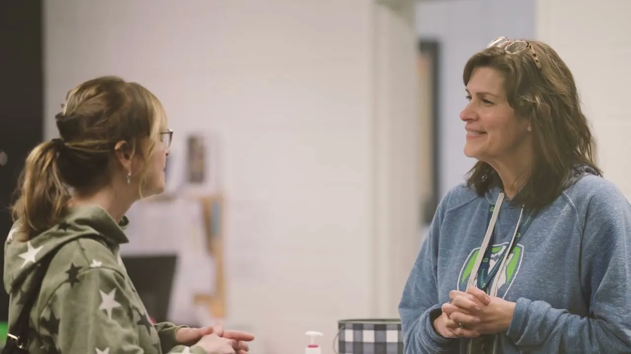 Two women talking together in a school classroom, one wearing a Eukarya sweatshirt